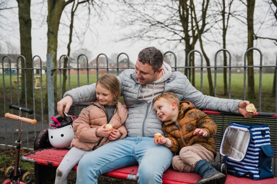 A dad in the ppark with two children eating apples