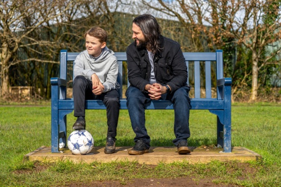 Man and boy sat on a bench with a football